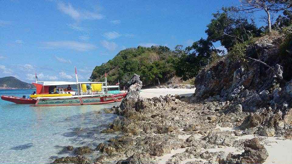 青い海とビーチに停泊するカラフルなボート、周囲には岩や緑の木々が見える風景